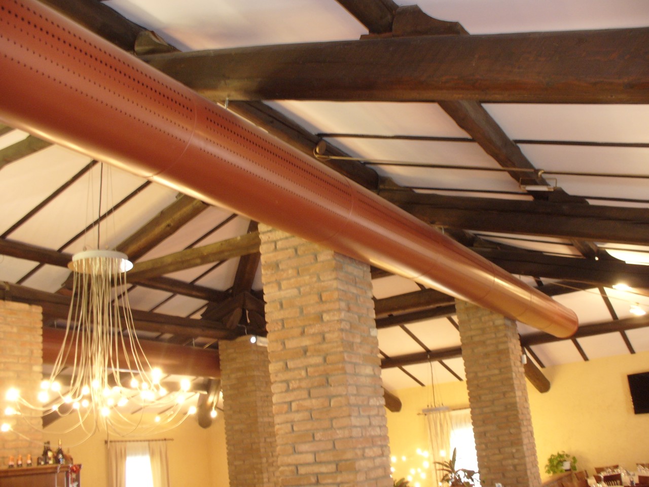 Canali microforati colorati a vista nel ristorante Desiderio, tra travi in legno e pilastri in mattoni